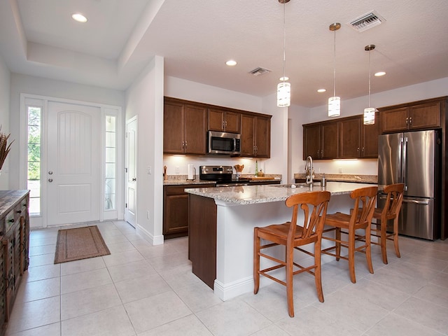 kitchen with light stone countertops, hanging light fixtures, an island with sink, and stainless steel appliances