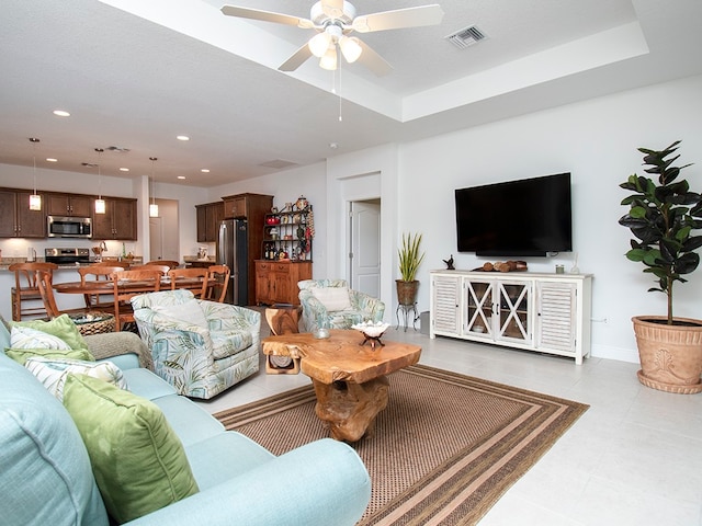 tiled living room featuring a textured ceiling, ceiling fan, and a raised ceiling