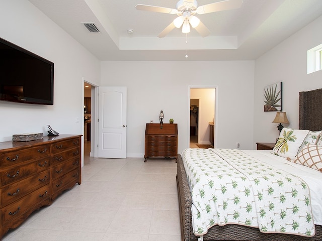 bedroom with connected bathroom, light tile patterned floors, ceiling fan, and a raised ceiling