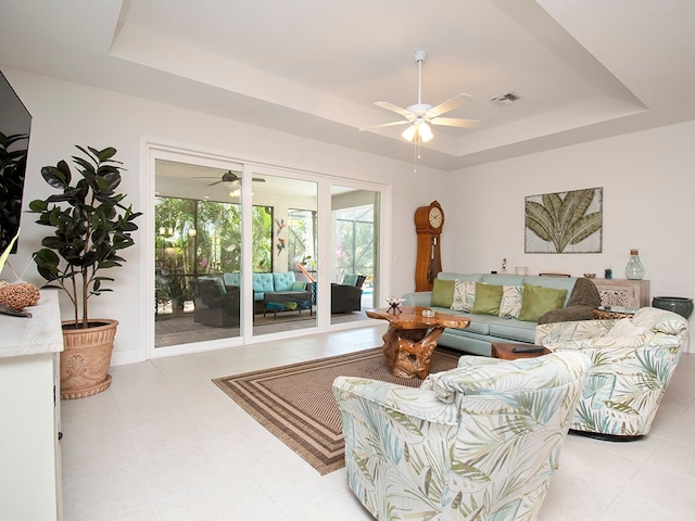 living room with light tile patterned flooring, ceiling fan, and a tray ceiling