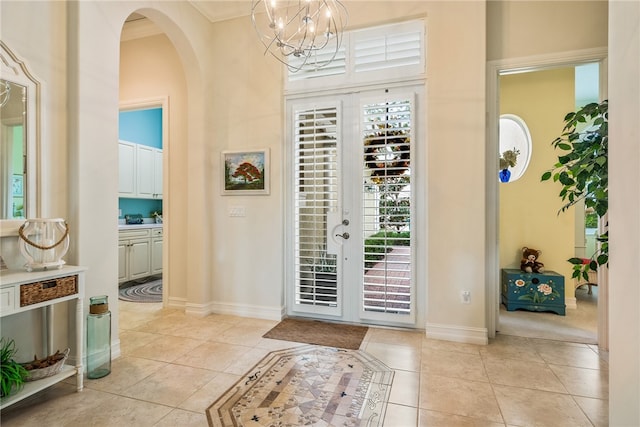 foyer with ornamental molding, a notable chandelier, and light tile patterned floors