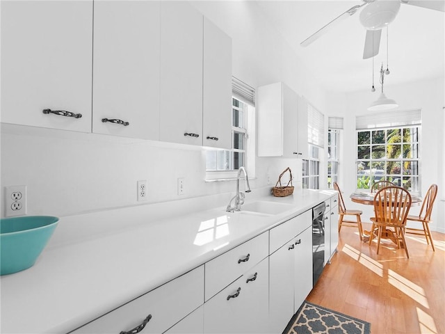 kitchen featuring sink, hanging light fixtures, black dishwasher, light hardwood / wood-style floors, and white cabinets