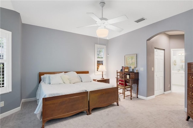 bedroom with arched walkways, light carpet, baseboards, and ensuite bathroom