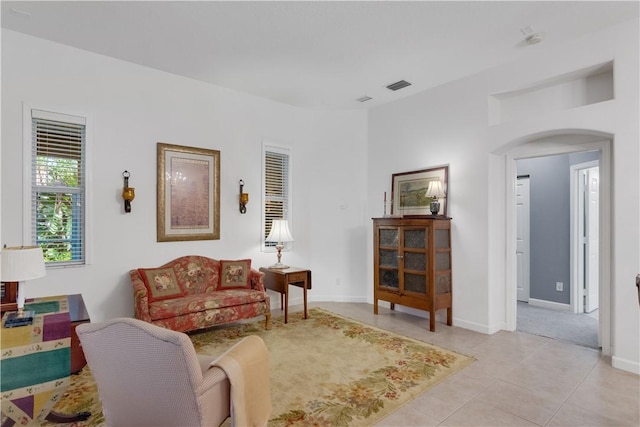 living area featuring arched walkways, light tile patterned floors, and baseboards