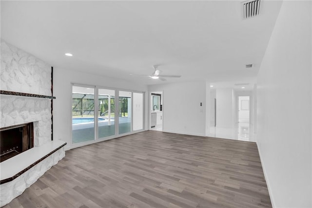 unfurnished living room featuring baseboards, visible vents, ceiling fan, wood finished floors, and a stone fireplace