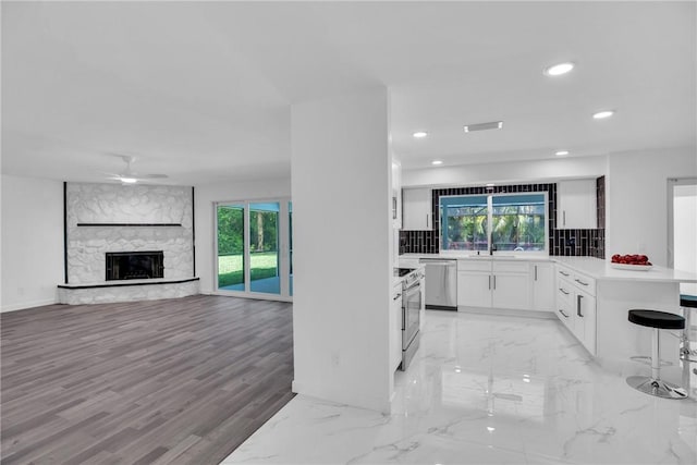 kitchen with a stone fireplace, a peninsula, white cabinets, light countertops, and tasteful backsplash