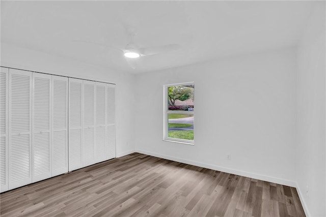 unfurnished bedroom featuring ceiling fan, a closet, baseboards, and wood finished floors