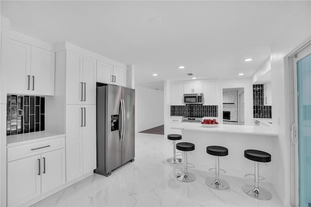 kitchen with marble finish floor, backsplash, appliances with stainless steel finishes, white cabinets, and a kitchen breakfast bar