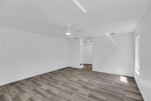 unfurnished room with ceiling fan, wood finished floors, visible vents, and baseboards