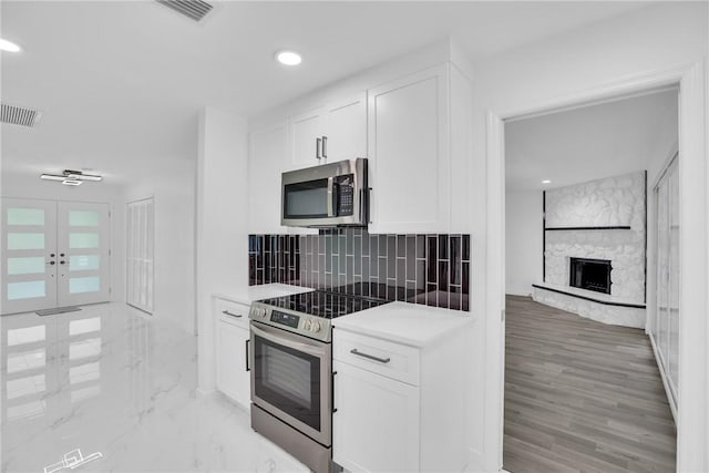 kitchen with a stone fireplace, visible vents, white cabinetry, appliances with stainless steel finishes, and decorative backsplash