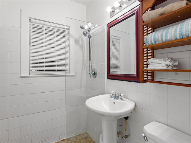 bathroom with toilet, tiled shower, and tile walls