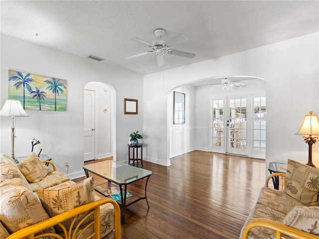 living room with a textured ceiling, ceiling fan, and dark wood-type flooring