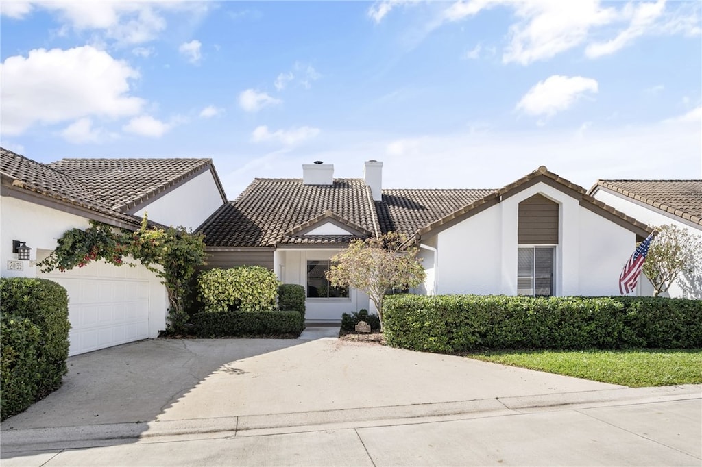 view of front of home featuring a chimney, stucco siding, a garage, driveway, and a tiled roof