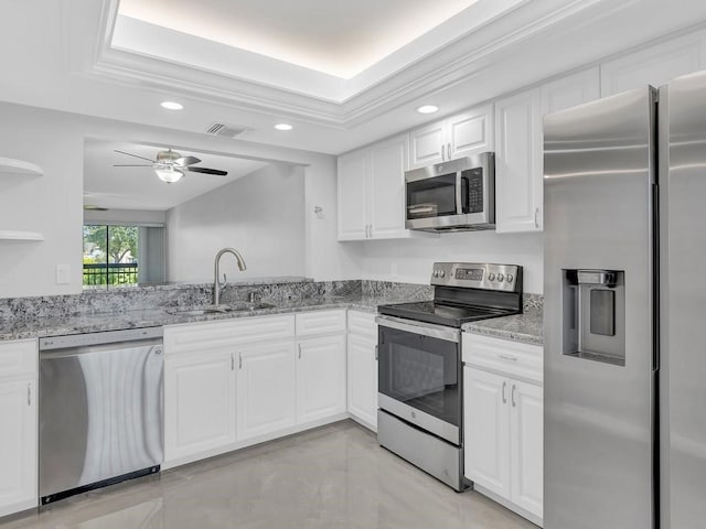 kitchen with stainless steel appliances, white cabinetry, a raised ceiling, and light stone counters