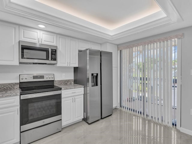 kitchen with white cabinets, stainless steel appliances, a tray ceiling, and light stone countertops