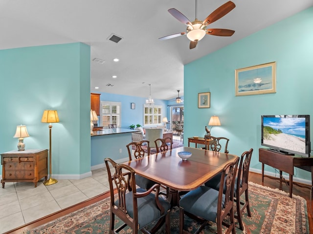 dining room with ceiling fan with notable chandelier, light tile patterned floors, and vaulted ceiling