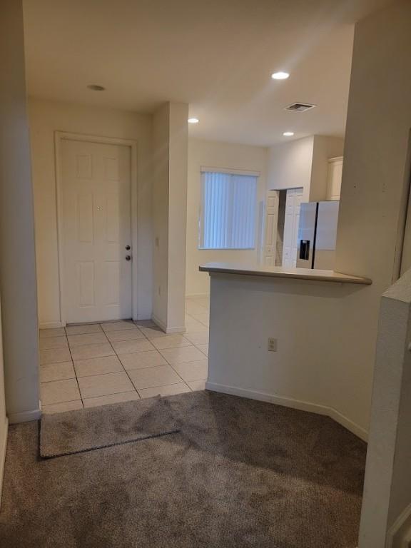 kitchen featuring stainless steel fridge with ice dispenser, light colored carpet, light tile patterned floors, baseboards, and a peninsula
