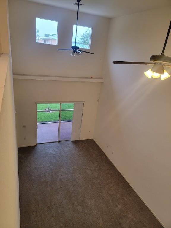 unfurnished living room with dark colored carpet, ceiling fan, and a high ceiling