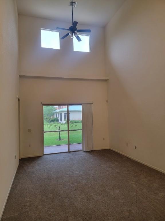 unfurnished living room with a high ceiling, carpet, ceiling fan, and baseboards