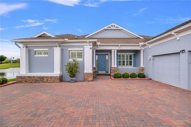 view of front of property with covered porch, stone siding, decorative driveway, and an attached garage