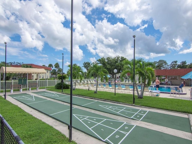 view of property's community featuring a pool, a lawn, shuffleboard, and fence