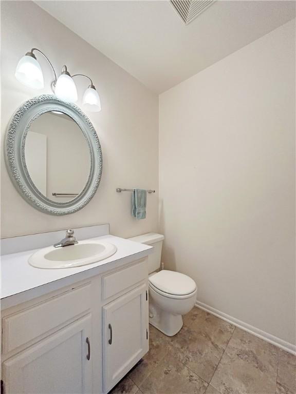 half bath with baseboards, visible vents, vanity, and toilet