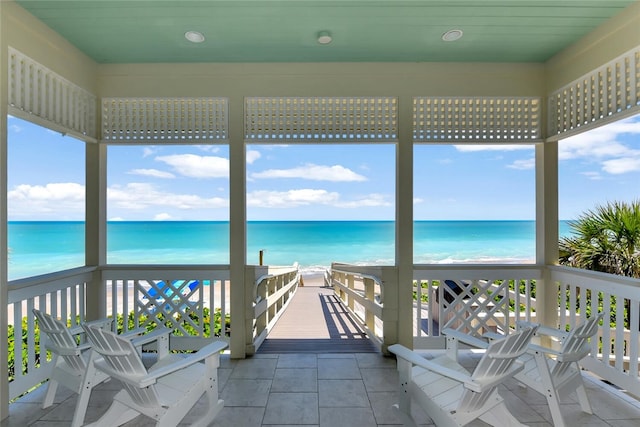 sunroom / solarium with a view of the beach, a water view, and tile patterned floors
