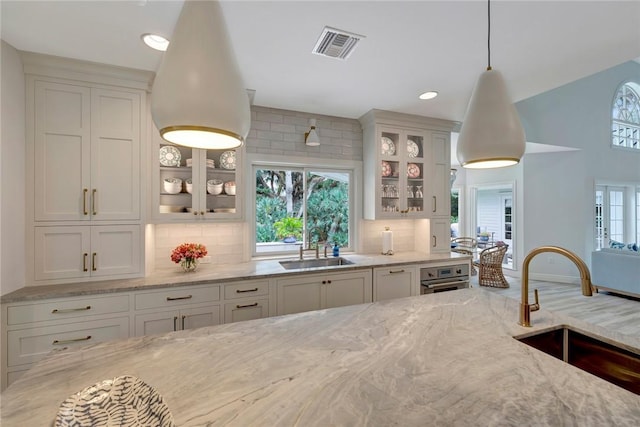 kitchen featuring decorative backsplash, visible vents, a sink, and light stone counters