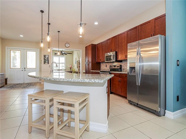 kitchen with french doors, decorative backsplash, appliances with stainless steel finishes, a kitchen island with sink, and a kitchen bar