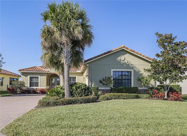 mediterranean / spanish home featuring a front yard, a tile roof, and stucco siding