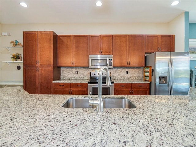 kitchen featuring appliances with stainless steel finishes, brown cabinetry, decorative backsplash, and light stone countertops