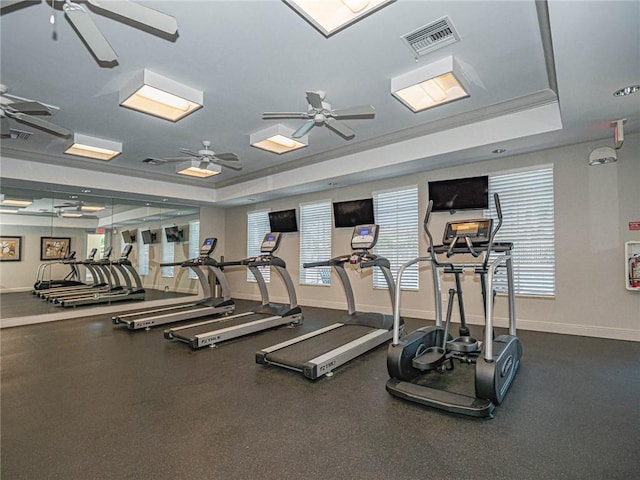 gym with a ceiling fan, a raised ceiling, visible vents, and baseboards