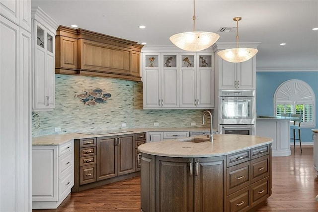 kitchen featuring sink, white cabinetry, hanging light fixtures, double oven, and a kitchen island with sink