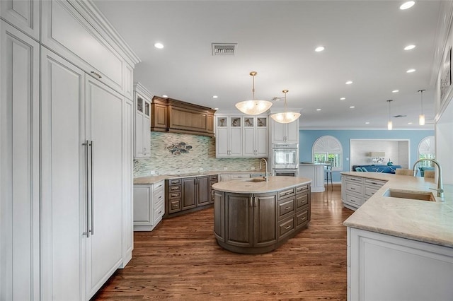 kitchen with white cabinetry, an island with sink, sink, hanging light fixtures, and dark wood-type flooring