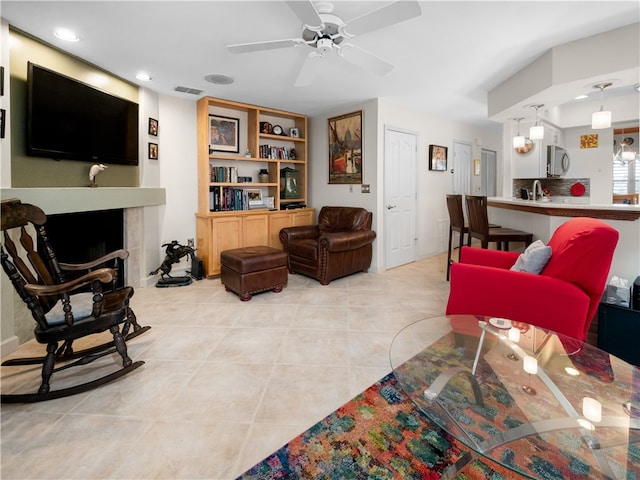 living room with ceiling fan, a tiled fireplace, and light tile patterned flooring