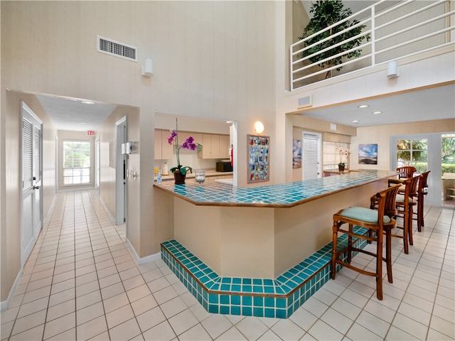 kitchen featuring a high ceiling, light tile patterned floors, a healthy amount of sunlight, and a breakfast bar area