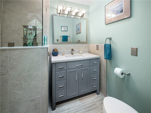 bathroom featuring walk in shower, vanity, toilet, and tile walls