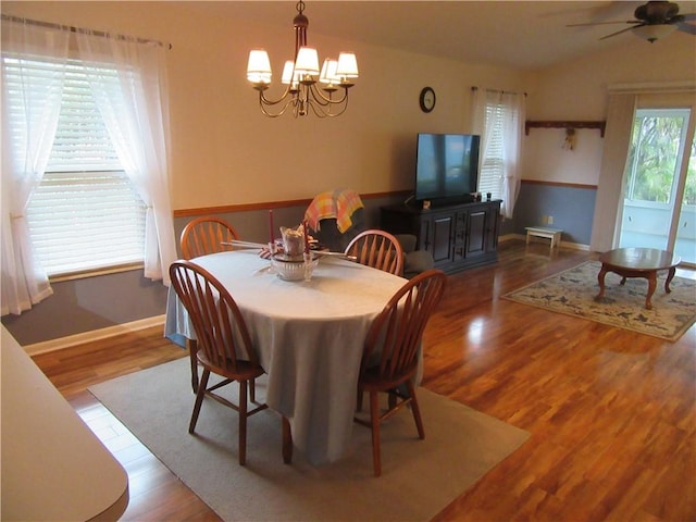 dining room with ceiling fan with notable chandelier, vaulted ceiling, wood finished floors, and baseboards