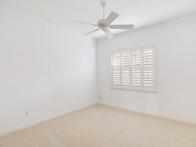 spare room with a ceiling fan, light colored carpet, and baseboards