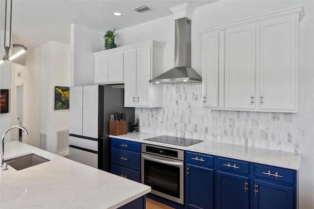 3612 2nd St SW, Vero Beach, FL 32968 - kitchen with stainless steel oven, wall chimney exhaust hood, black electric stovetop, blue cabinetry, and recessed lighting