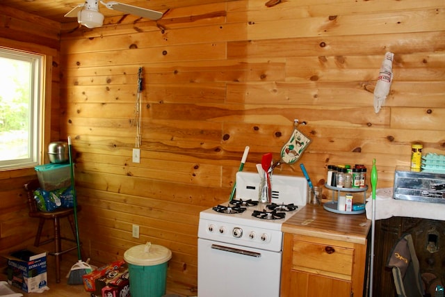 kitchen with wood walls, white gas range, and ceiling fan