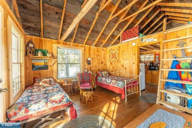 bedroom with white refrigerator, wood walls, hardwood / wood-style floors, and lofted ceiling