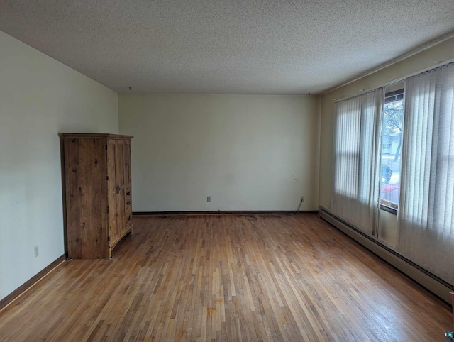 spare room with hardwood / wood-style flooring, a baseboard heating unit, and a textured ceiling