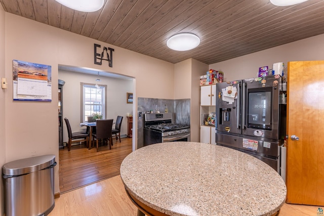 kitchen featuring stainless steel range with gas cooktop, light wood-type flooring, black fridge, wood ceiling, and tasteful backsplash