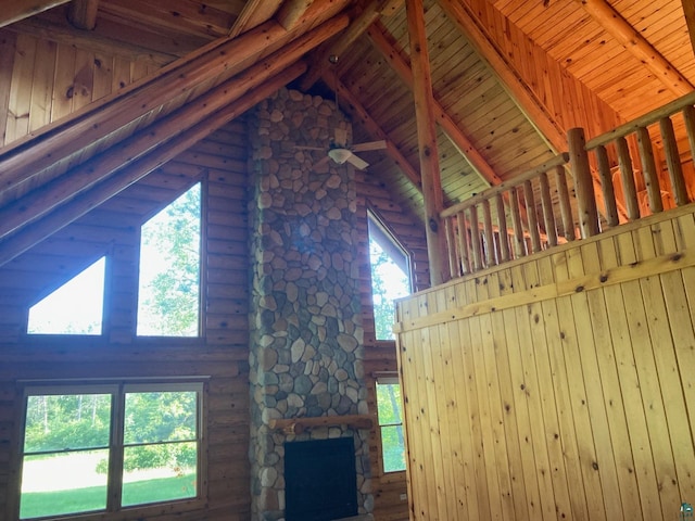 unfurnished living room featuring wooden ceiling, high vaulted ceiling, a stone fireplace, rustic walls, and beamed ceiling