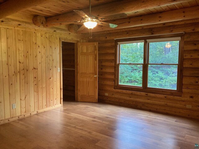 spare room featuring beam ceiling, rustic walls, ceiling fan, wood ceiling, and light wood-type flooring