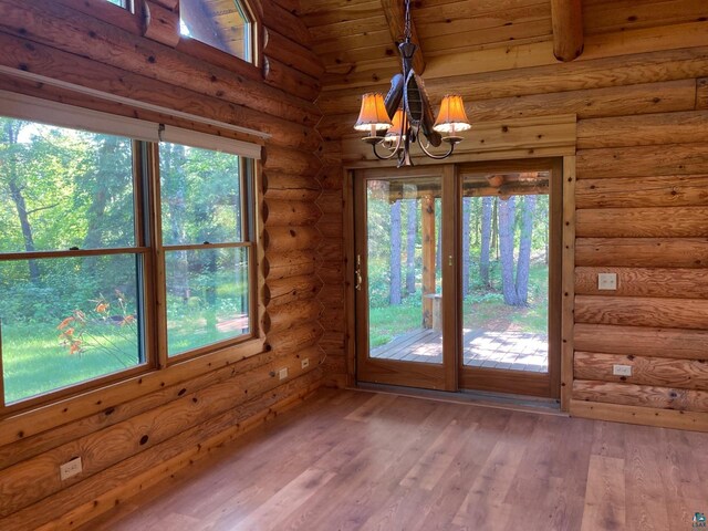 unfurnished dining area with log walls, hardwood / wood-style floors, an inviting chandelier, and a wealth of natural light