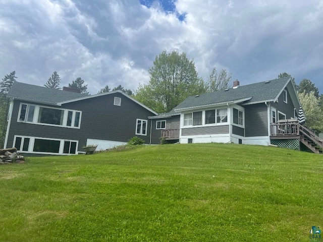 back of property featuring a sunroom, a wooden deck, and a lawn