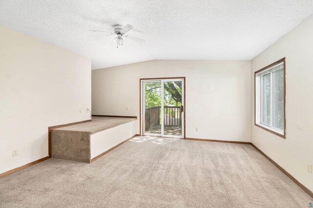 carpeted empty room featuring ceiling fan, vaulted ceiling, and a textured ceiling