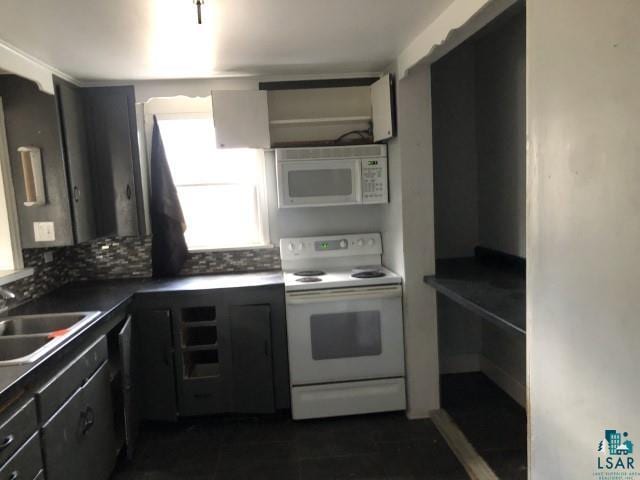 kitchen with dark tile patterned flooring, backsplash, white appliances, and sink